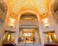 Interior view of a grand arched hallway with ornate ceiling and walls, featuring statues and visitors.