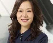Portrait d'une femme souriante aux longs cheveux ondulés, vêtue d'une chemise à boutons bleu foncé.
