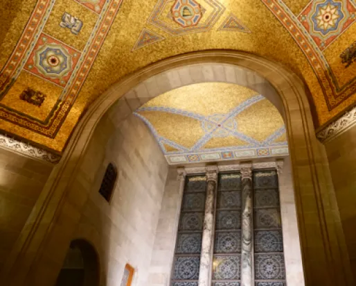 Ornate architectural ceiling with gold mosaic tiles and a large arched stone entryway beneath it.