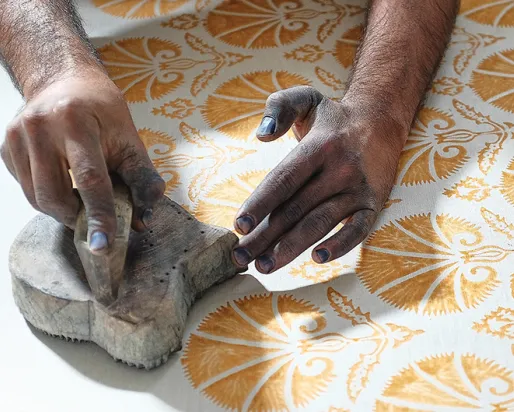 Les mains pressent un tampon avec de la peinture jaune sur un tissu blanc.
