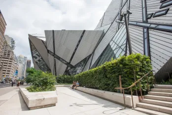 Modern angular glass and metal building with outdoor concrete planters and stairs surrounded by greenery.