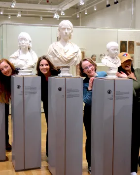 "Un groupe de personnes pose de manière ludique en se penchant entre des bustes de marbre classiques dans une galerie de musée.