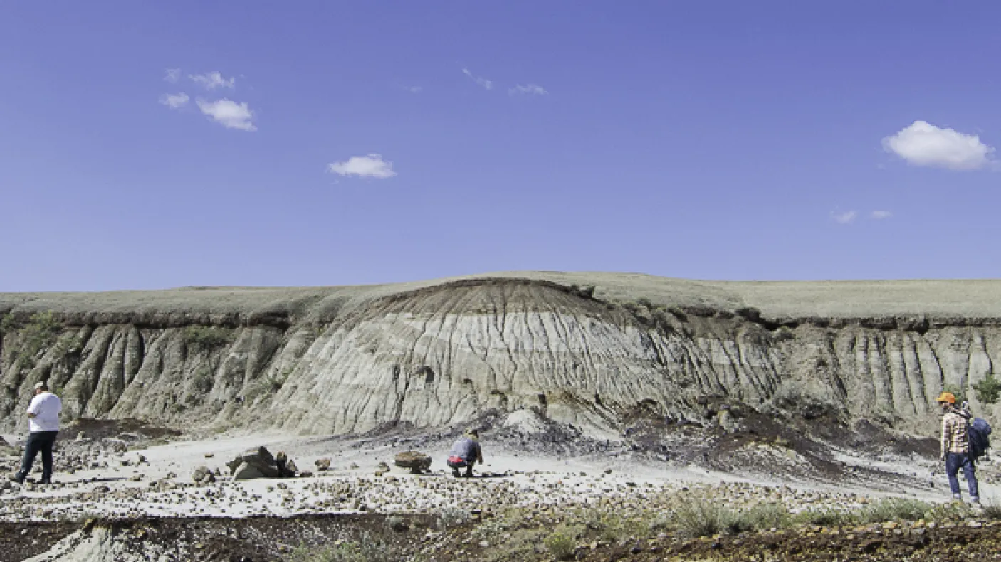 Four people scattered across a rocky, layered cliff landscape under a blue sky with a few clouds.