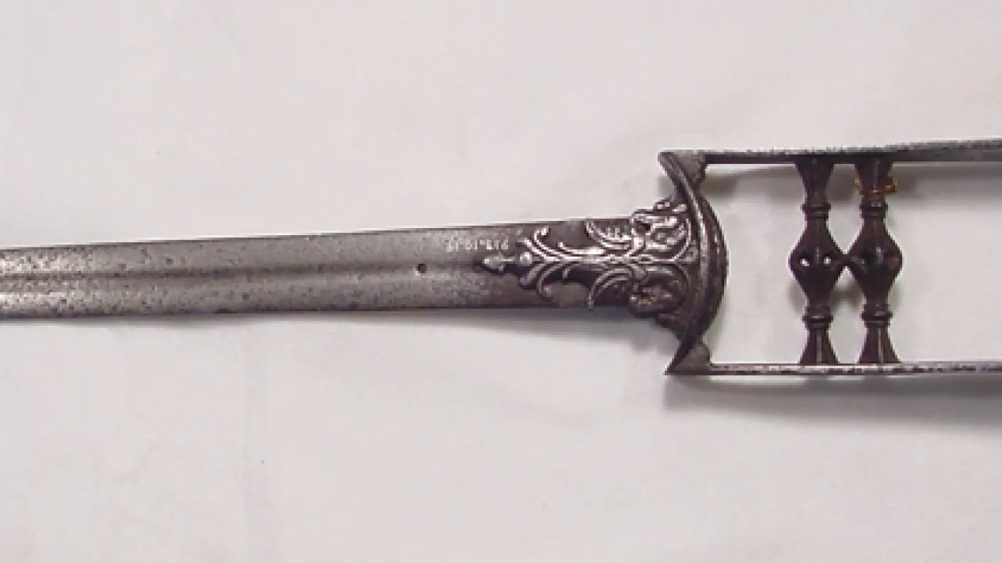 Metal two-pronged fork with ornamental handle featuring floral engravings.