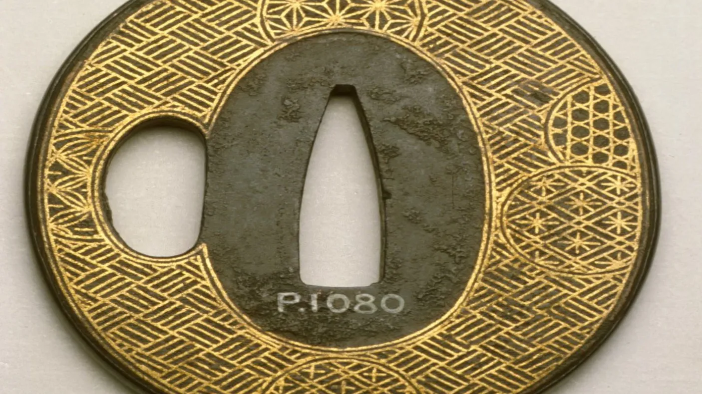 Circular Japanese sword guard with intricate gold and black geometric patterns and a central cutout.
