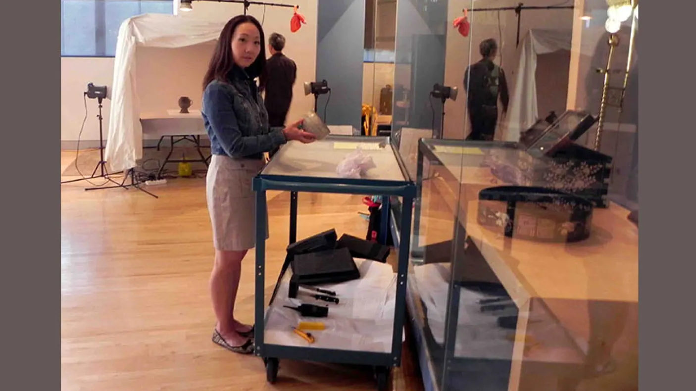A woman standing next to a desk with a box on it inside a museum gallery space.
