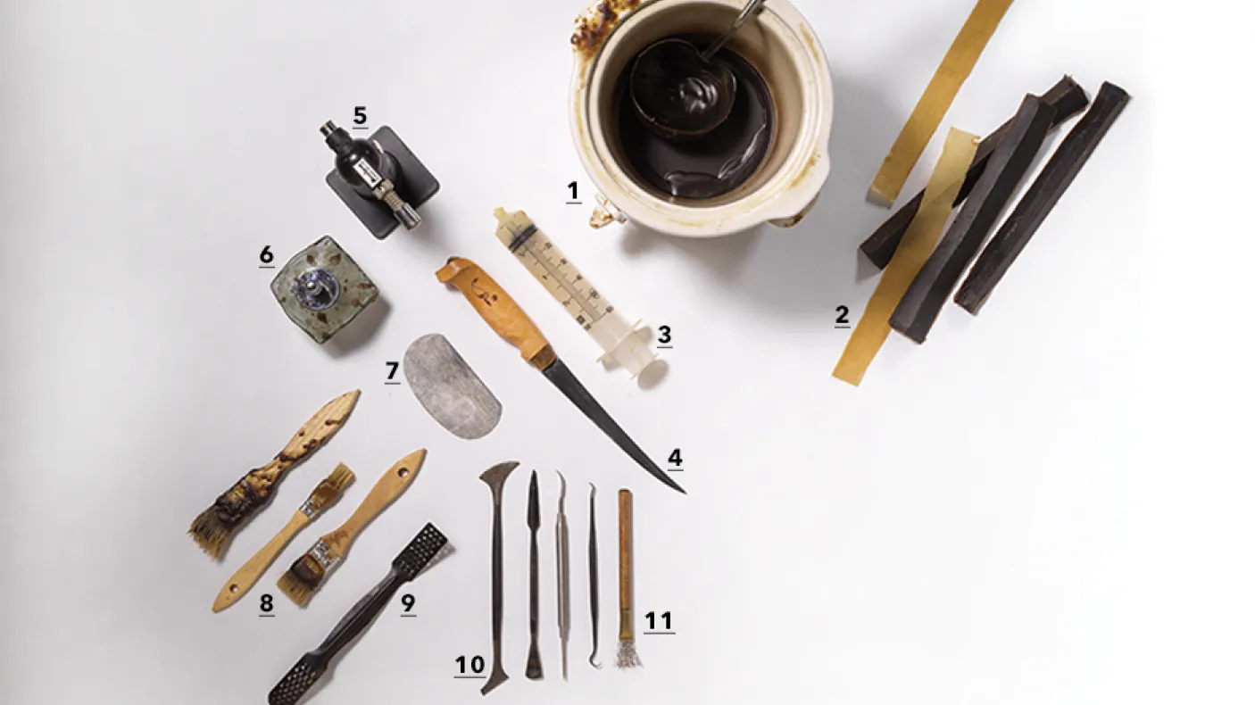 Various traditional tools including knives, scrapers, and small carved objects arranged on a white surface alongside a cup of coffee.