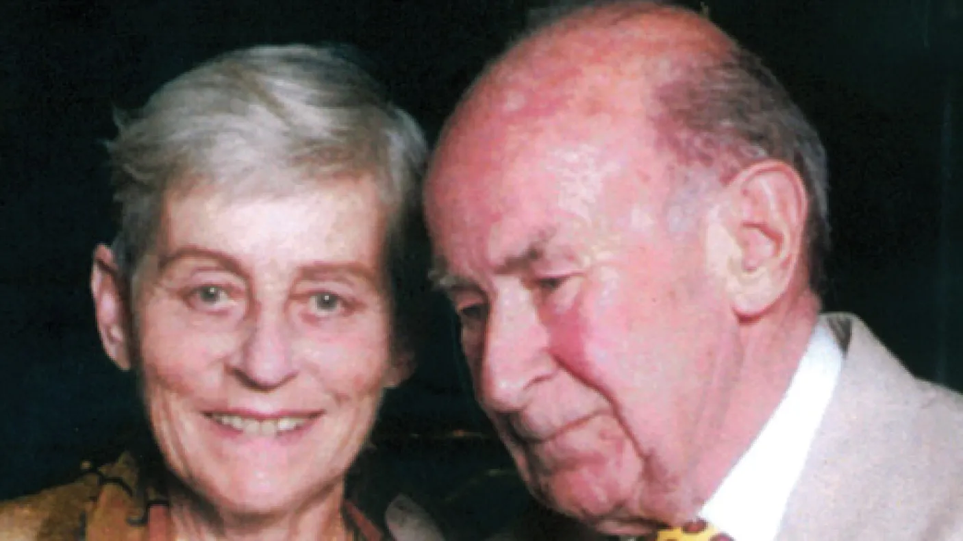 Portrait of an elderly woman with short gray hair smiling, beside an elderly bald man with a yellow tie and suit.