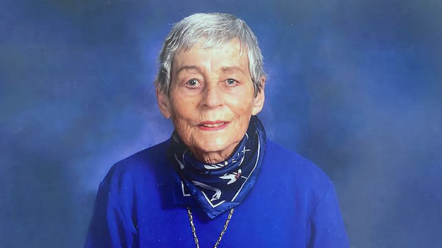 Portrait of an older woman with short gray hair, wearing a blue sweater and a patterned scarf.