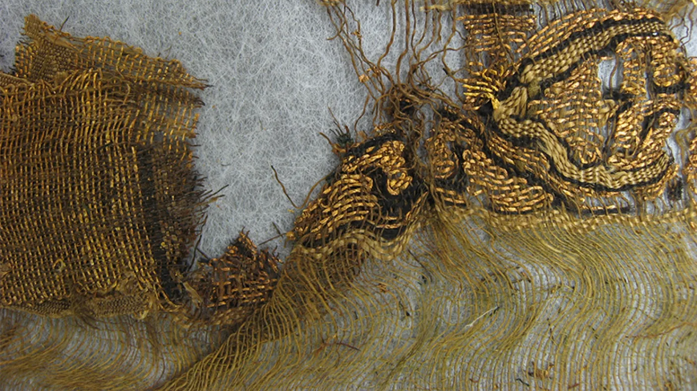 Fragment de textile ancien montrant des fils lâches et une étoffe tissée dans des tons bruns et beiges.