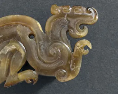 Carved jade dragon-shaped ornament with curving body and detailed facial features.