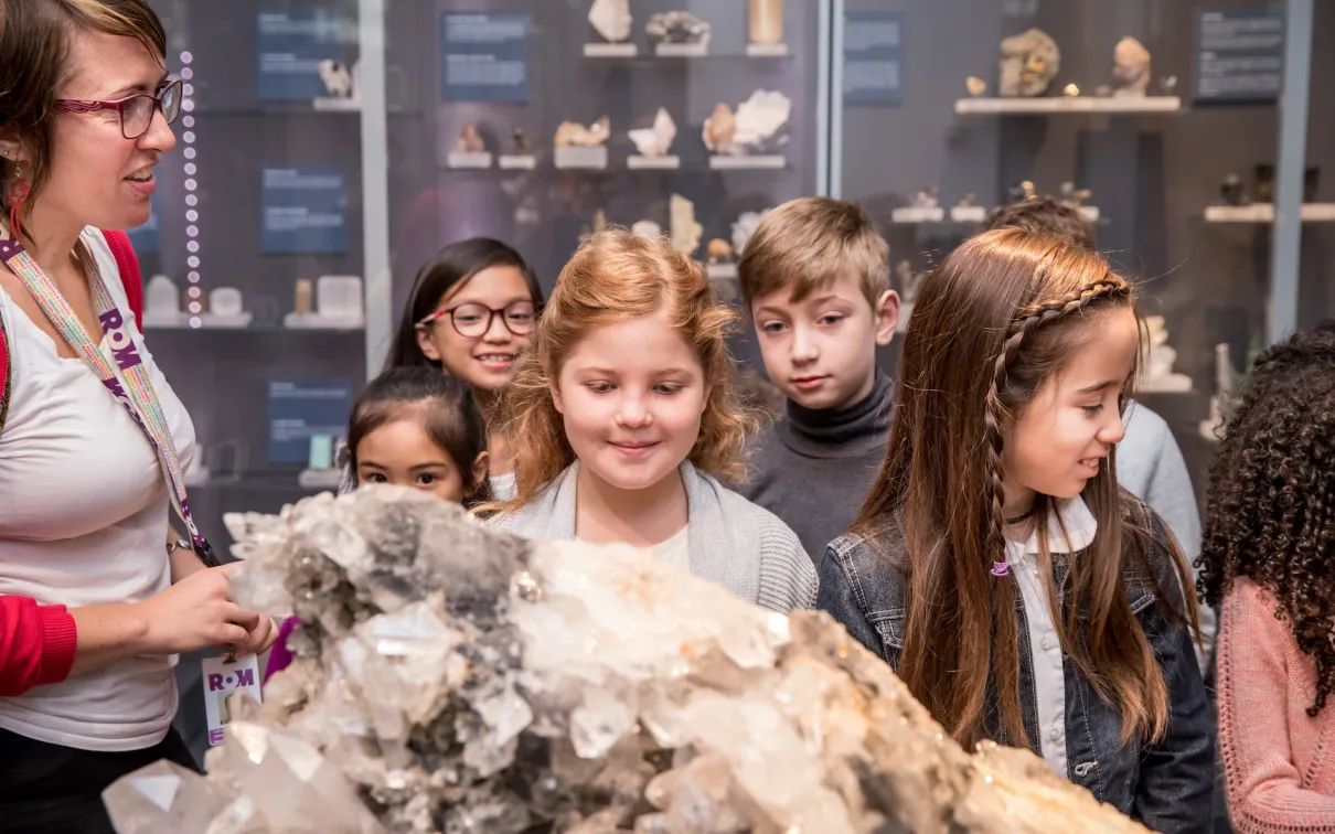 A group of children and an adult are gathered around a large mineral or crystal display in a museum exhibit.