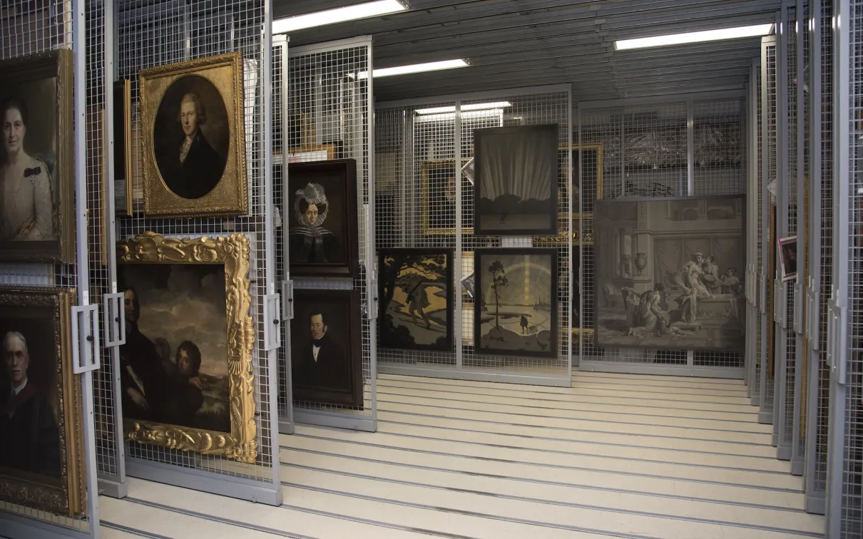 A storage area with art pieces on racks including framed paintings and portraits in a museum setting.