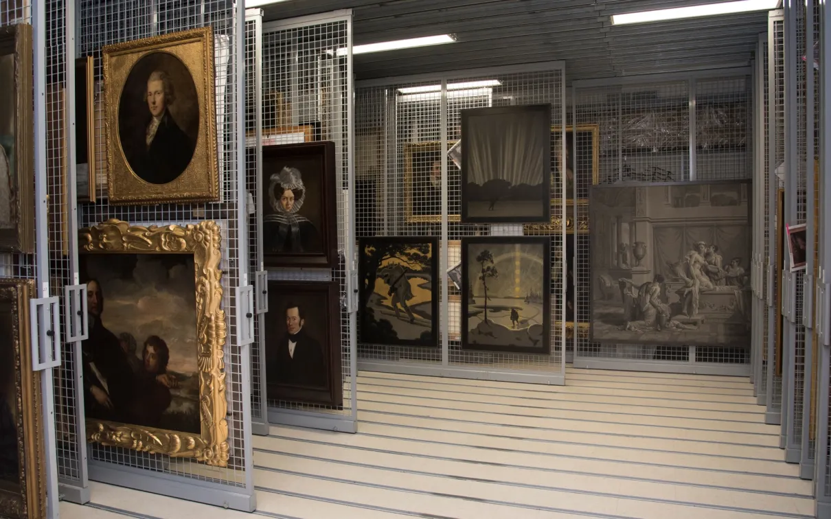 Interior view of a museum storage area with artworks and paintings on metal racks.