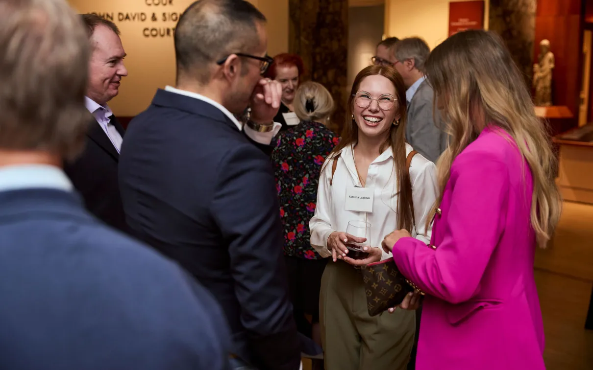 A group of adults socializing indoors, with one woman holding a wine glass and smiling.