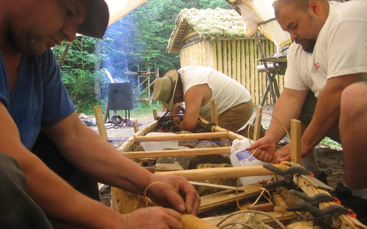 Trois hommes fabriquant un canoë en écorce de bouleau.