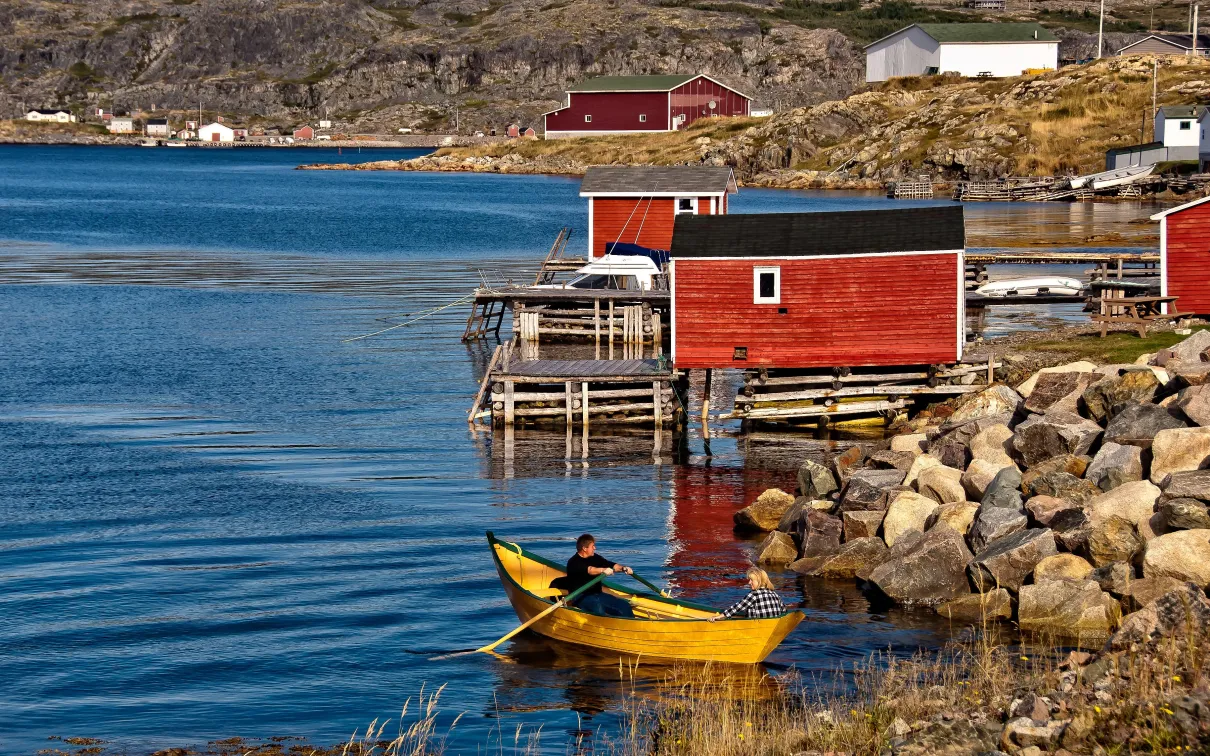 Maisons colorées au bord de la mer avec une barque au premier plan.