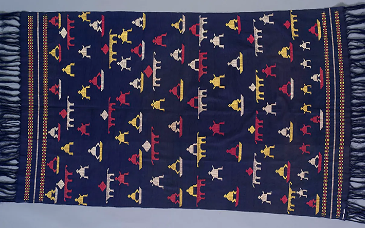 Textile tissé avec un fond bleu foncé et des motifs géométriques en rouge, jaune, blanc et bleu avec des bords frangés.
