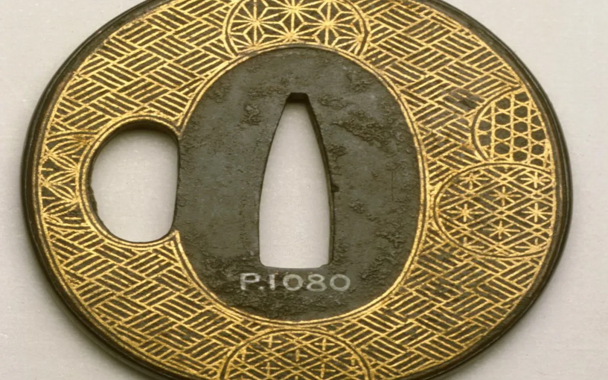 Circular Japanese sword guard with intricate gold and black geometric patterns and a central cutout.