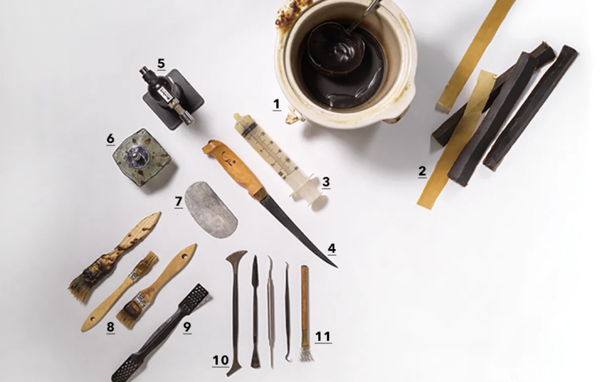 Various traditional tools including knives, scrapers, and small carved objects arranged on a white surface alongside a cup of coffee.