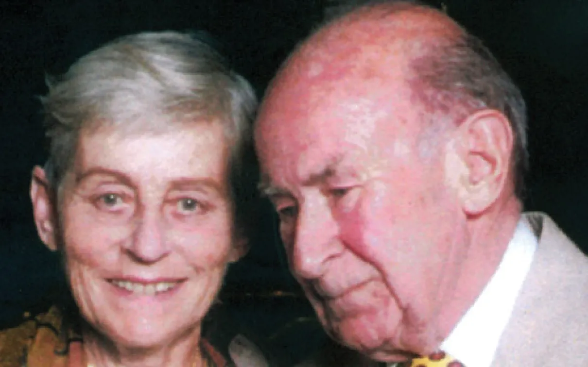 Portrait of an elderly woman with short gray hair smiling, beside an elderly bald man with a yellow tie and suit.