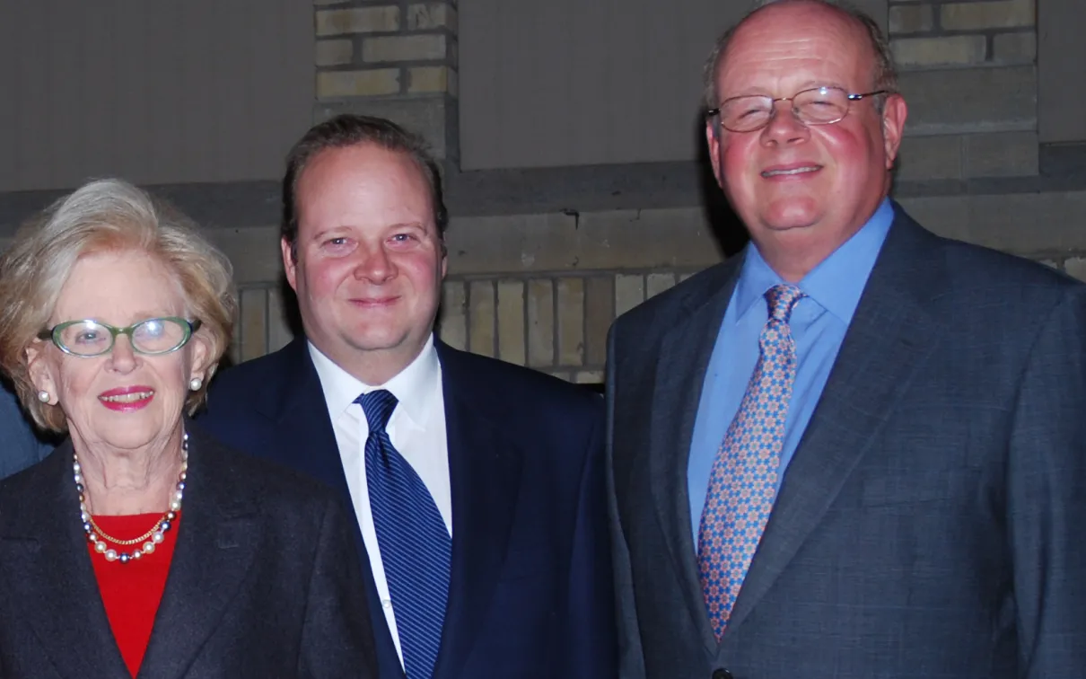 Three people posing closely together, all wearing formal attire against a neutral indoor background.