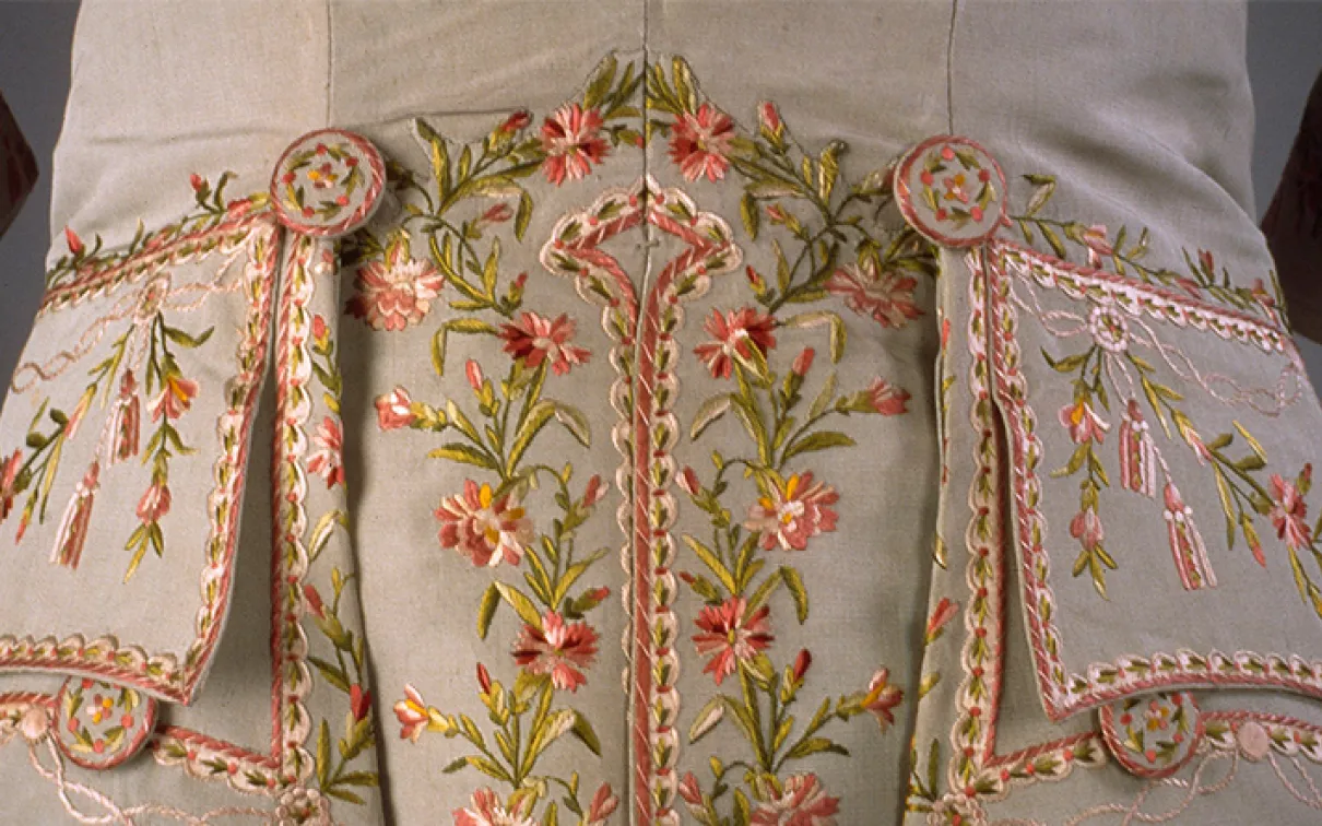 Gros plan sur un tissu beige brodé de motifs floraux roses et verts et décoré de perles.