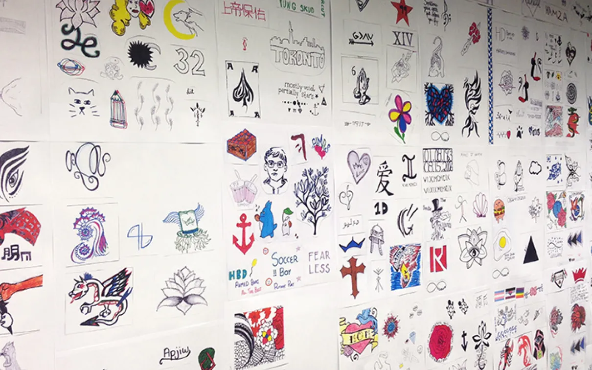 Hundreds of tattoo designs on white paper are posted on a wall