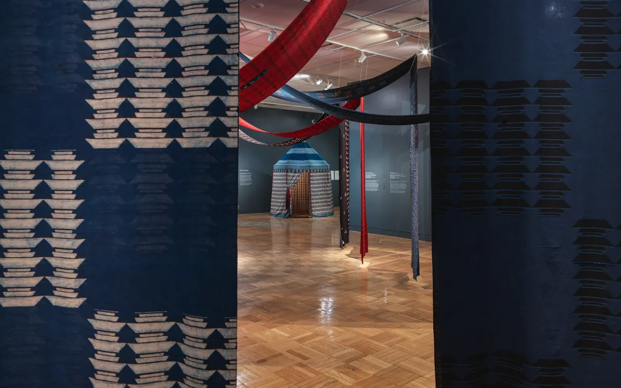 View of a cotton tent structure seen through a break in two printed, hanging cotton panels in the exhibition Swapnaa Tamhane: Mobile Palace, at ROM.