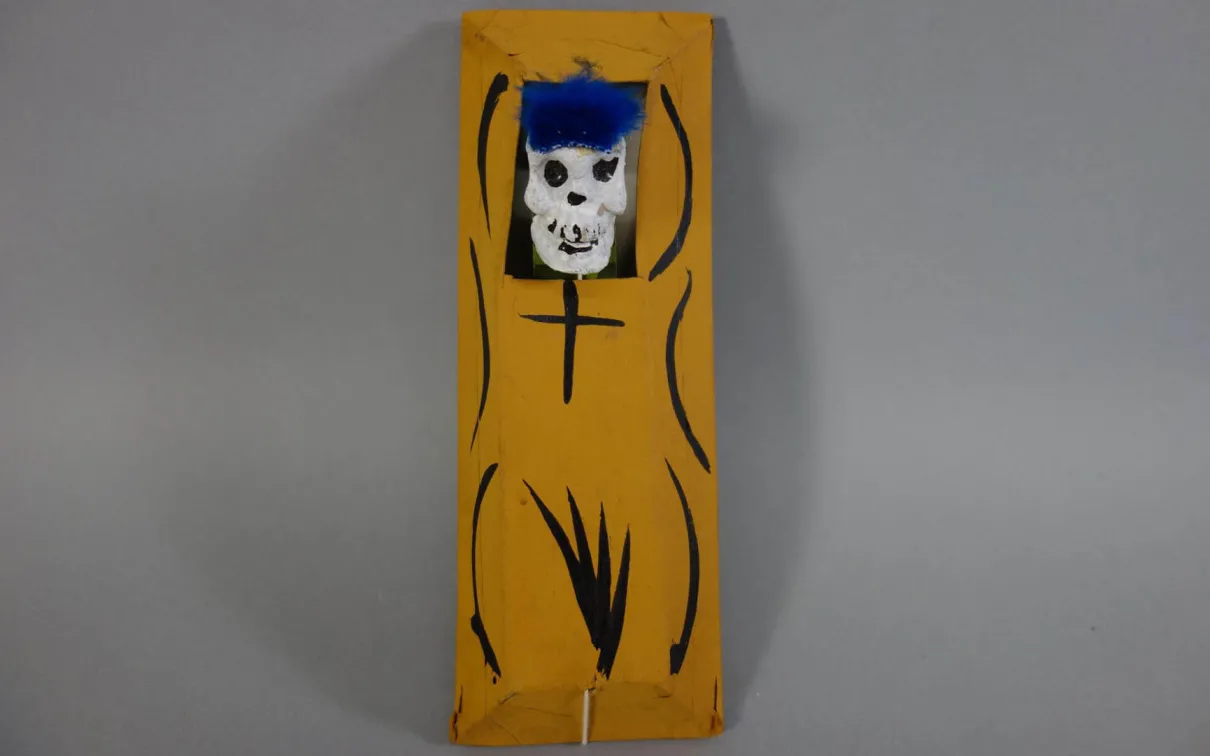 Objet rectangulaire jaune avec des lignes courbes noires et un petit crâne blanc au sommet.