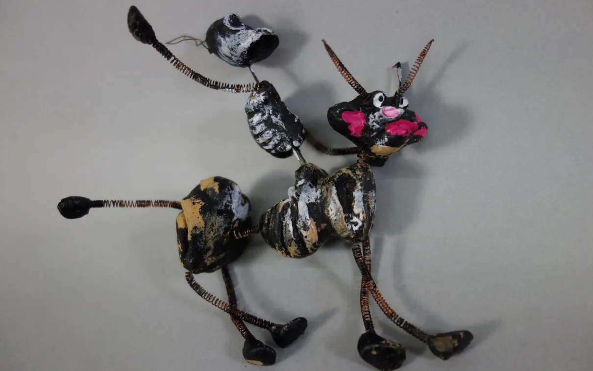 Petit animal en brindilles et bâtons peints sur fond gris.