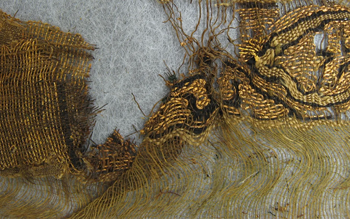 Fragment de textile ancien montrant des fils lâches et une étoffe tissée dans des tons bruns et beiges.