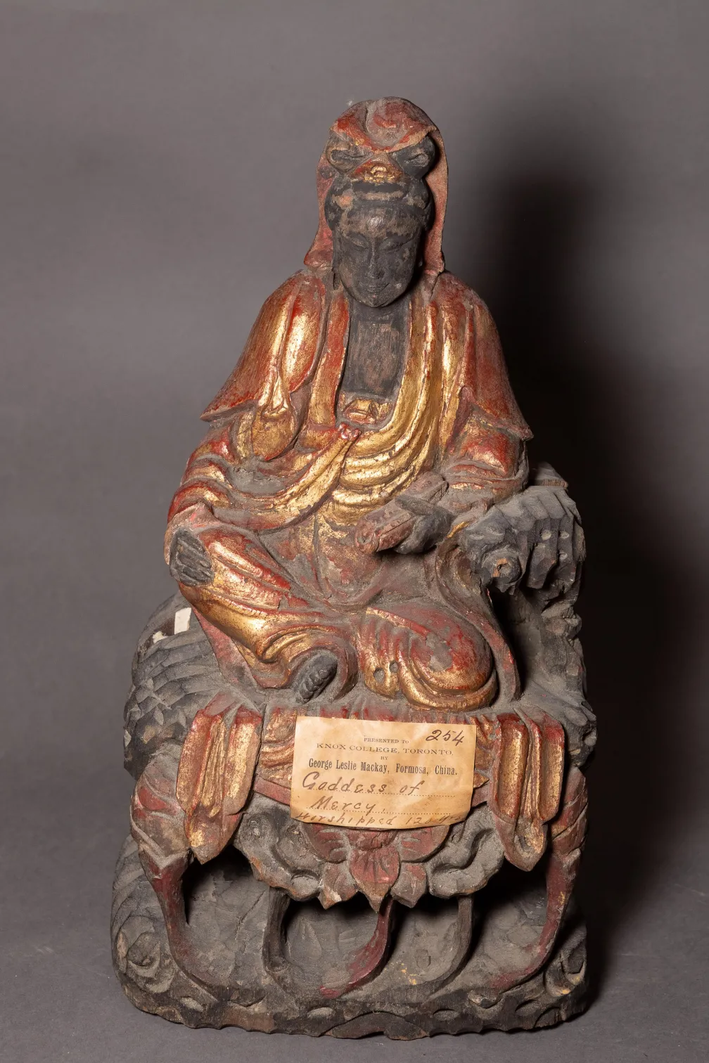 Seated figure statue with a beard, wearing a robe and holding an object, with a worn label on the base.