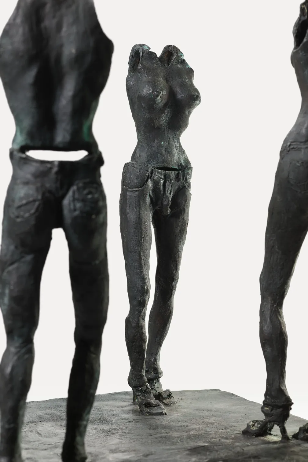 Three dark bronze abstract sculptures of human torsos standing on a flat base.