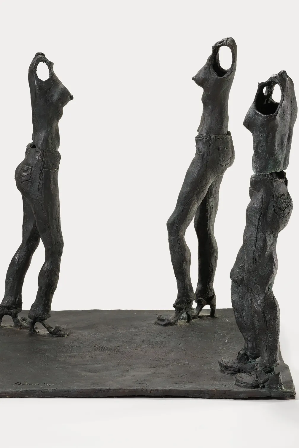 Bronze sculpture of three standing female figures with stylized, elongated forms on a flat base.