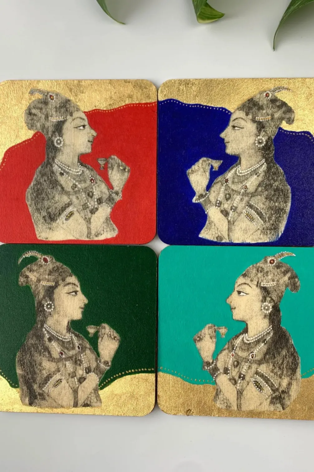 Four square coasters each featuring a stylized profile of a woman wearing a headpiece and holding a flower, with red, blue, dark green, and teal backgrounds.