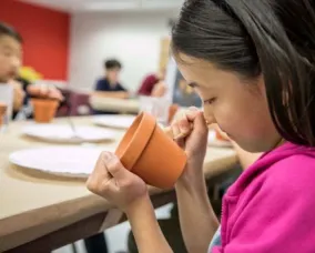 Un élève de l'espace de création ROM dessine au crayon sur un pot d'argile.