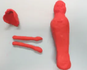 Red modeling clay shaped into a rough head, a flat rectangular piece, two long cylindrical pieces, and a tall, rounded figure.