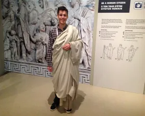 The young man stands with his left arm holding the toga in place.