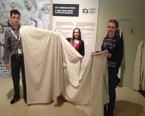 One end of the piece of white fabric hangs over the young man’s shoulder and covers his entire arm. The young women hold the rest of the fabric.