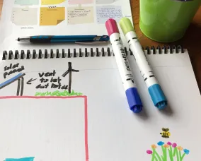 A coloured version of the sustainable school design. Several markers sit on the paper.