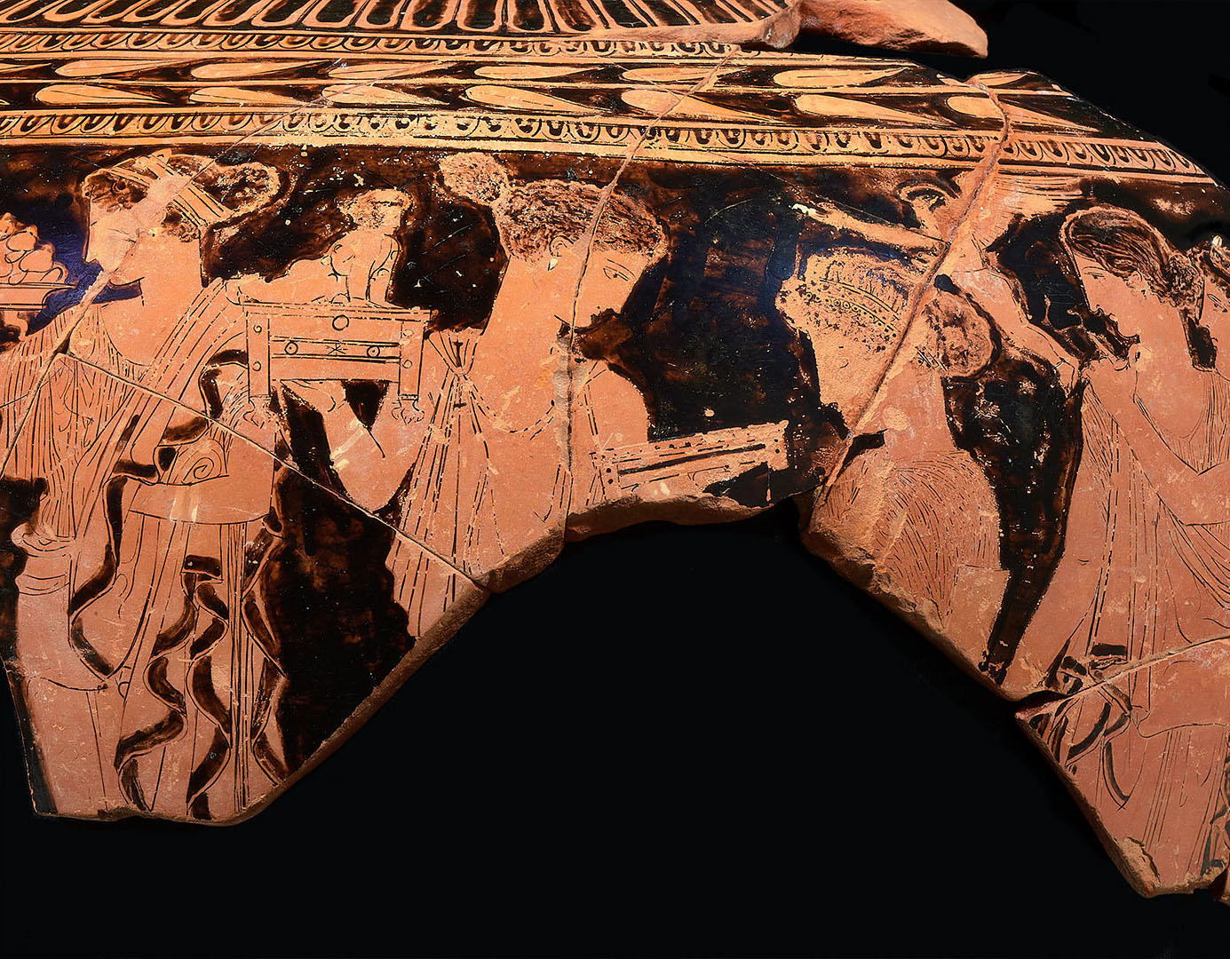 Fragment d'un vase grec à figures rouges représentant trois figures humaines drapées, dont l'une tient un bâton ou une lance.